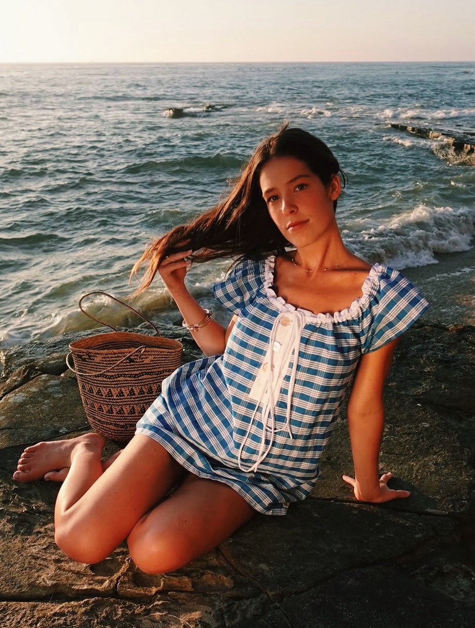 Portrait of Savannah Ames in a blue dress by the ocean, smiling at the camera